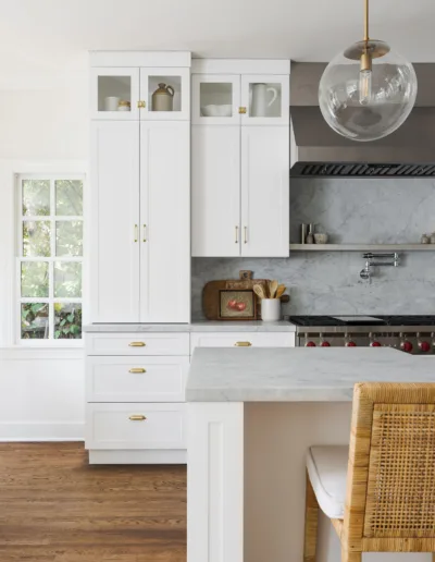 A white kitchen with wooden floors and a wicker chair.
