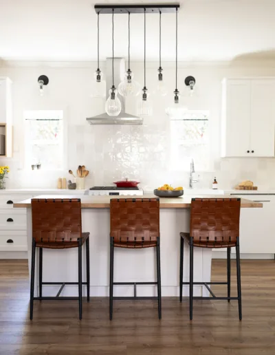 A white kitchen with wooden floors and leather stools.